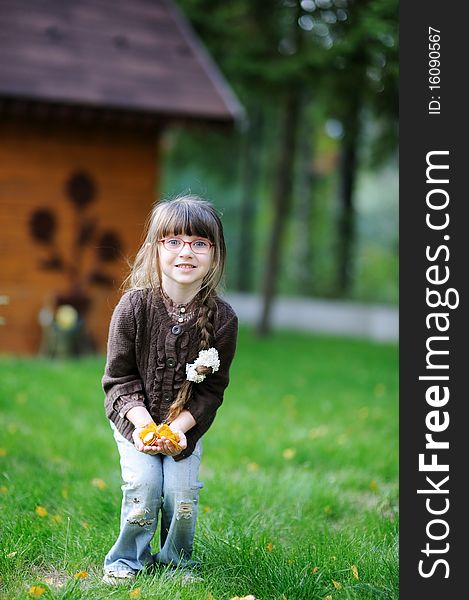 Adorable little girl plays with yellow leaves in the yard