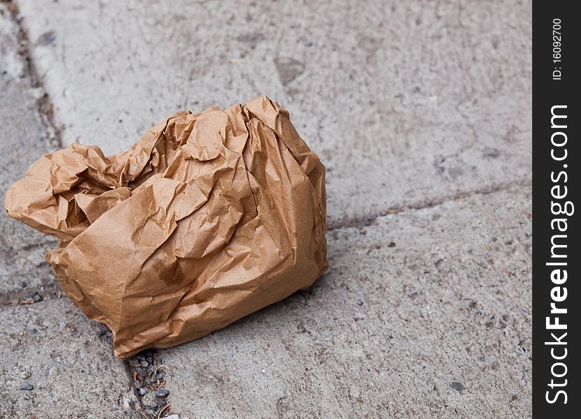 Crumpled brown paper bag discarded on a sidewalk. Crumpled brown paper bag discarded on a sidewalk