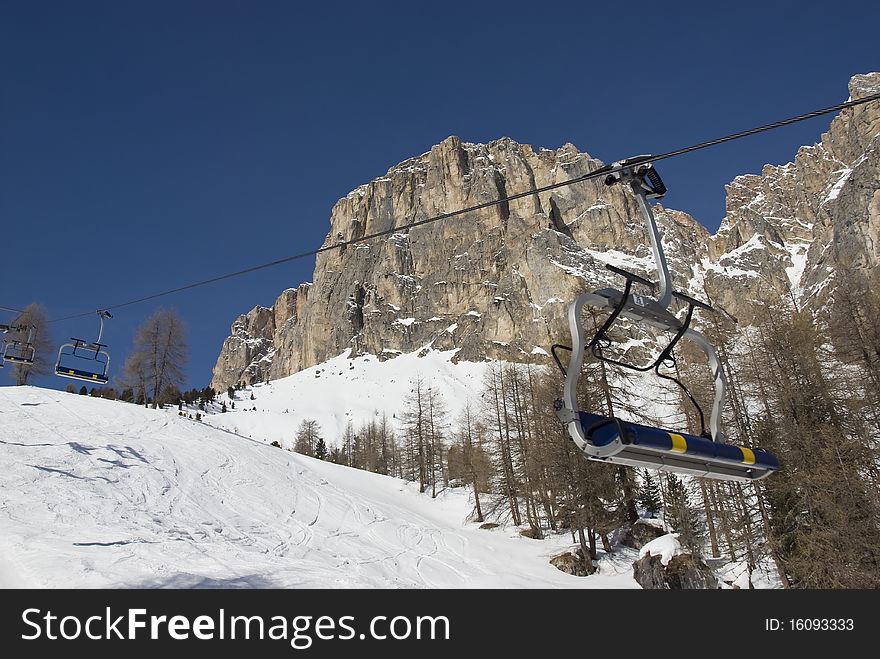 Empty chair lift in a skiing resort with mountains and blue sky in the background. Val gardena, Dolomites, Italy. Empty chair lift in a skiing resort with mountains and blue sky in the background. Val gardena, Dolomites, Italy.