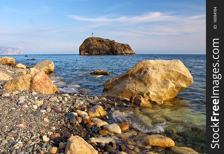 A lonely rock with a cross standing in the sea near the coast. A lonely rock with a cross standing in the sea near the coast