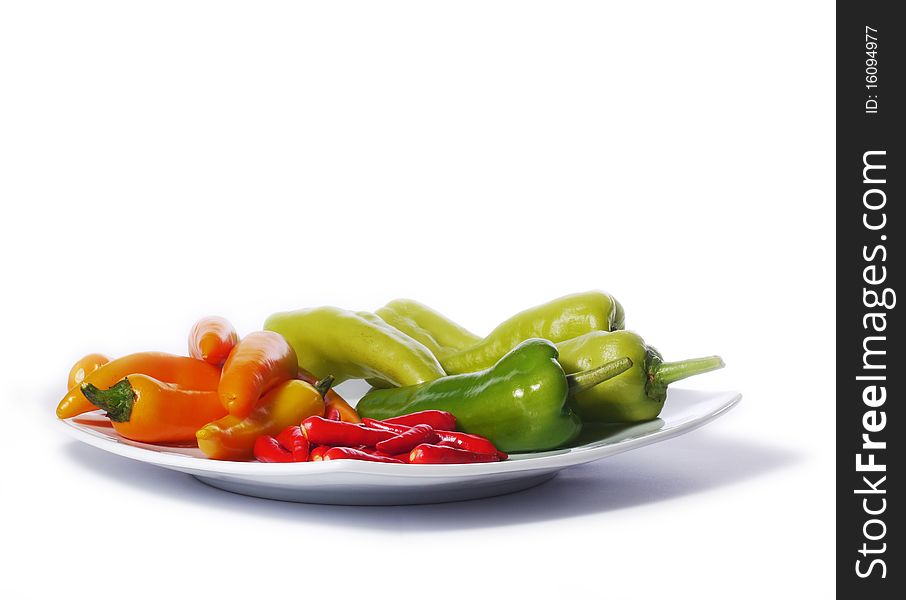 Red, orange and green chili peppers from Thailand on a white plate. Isolated on white. Red, orange and green chili peppers from Thailand on a white plate. Isolated on white.