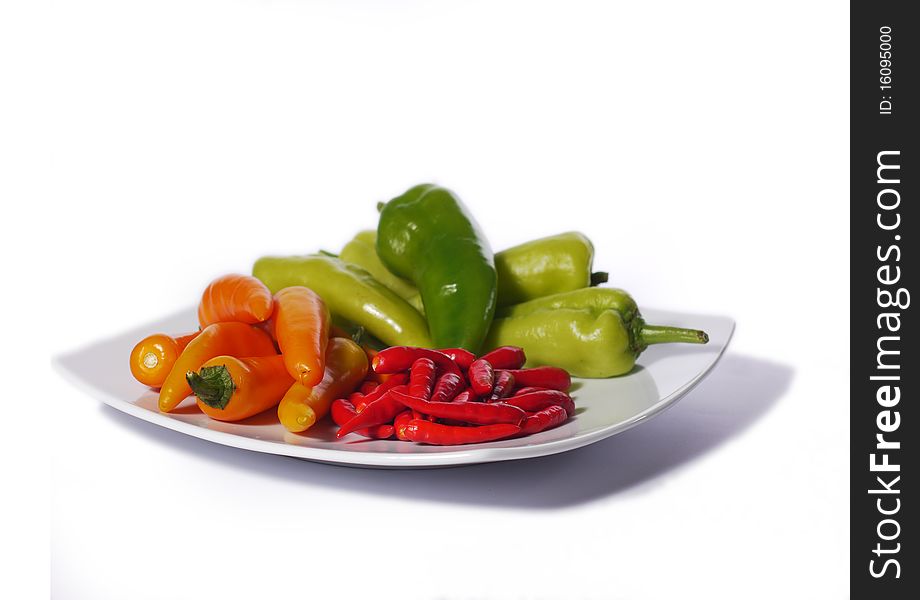 Red, orange and green chili peppers from Thailand on a white plate. Isolated on white. Shallow depth of field with the nearest peppers in focus. Red, orange and green chili peppers from Thailand on a white plate. Isolated on white. Shallow depth of field with the nearest peppers in focus.