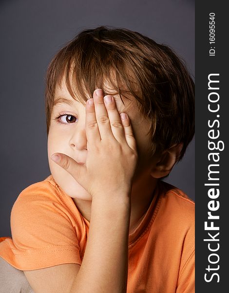 Portrait of cute little boy playing hide-and-seek, studio shot