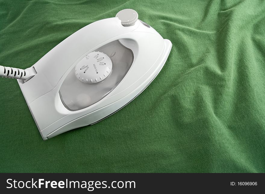 White electric iron on green cotton cloth. White electric iron on green cotton cloth.