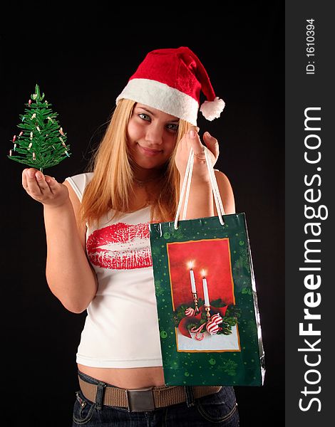 Christmas blonde girl offer a little Christmas-tree and a gift in a bag, black background. Christmas blonde girl offer a little Christmas-tree and a gift in a bag, black background