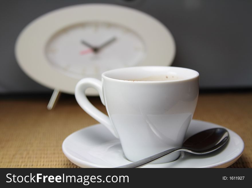 Cup of Cappucino coffee in White Cup and with Spoon and Clock as background