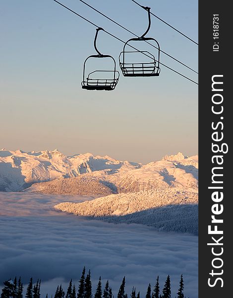An empty chairlift takes riders high in the sky over mountains and valley clouds.