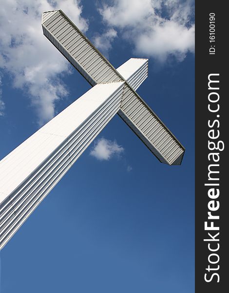 A massive modern cross slants against a cloudy blue sky. A massive modern cross slants against a cloudy blue sky.