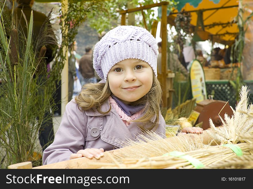 The girl in a violet raincoat and a cap costs near a cart with wheat crop. The girl in a violet raincoat and a cap costs near a cart with wheat crop