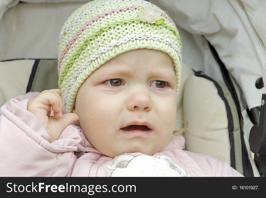 The small child in outer clothing sits in a children's carriage and cries. The small child in outer clothing sits in a children's carriage and cries