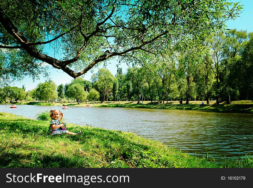 Cute happy toddler girl sitting on river bank with toys. Cute happy toddler girl sitting on river bank with toys