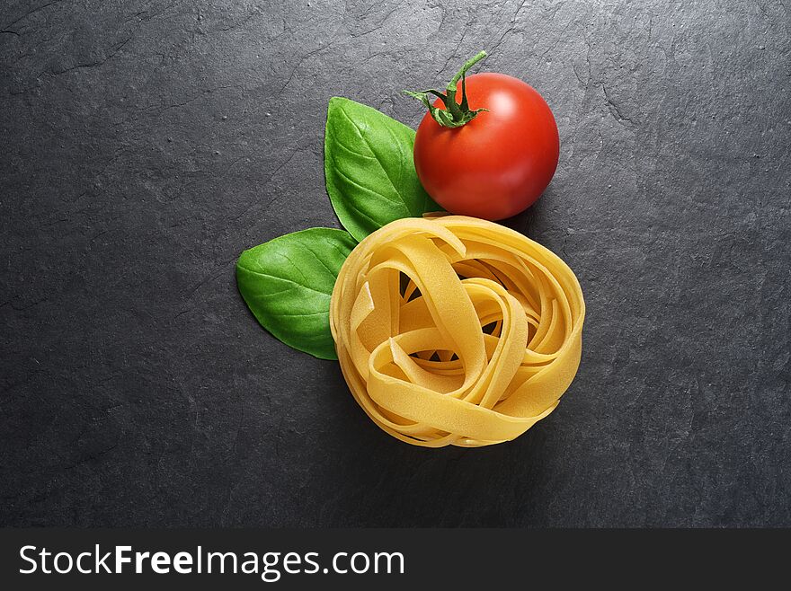 Fettuccine pasta with basil leaves and tomato on black slate background with copy space. Fettuccine pasta with basil leaves and tomato on black slate background with copy space