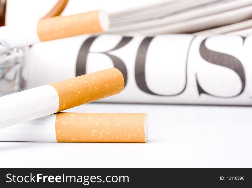 Filtered cigarettes laying in front of a newspaper and an ashtray.