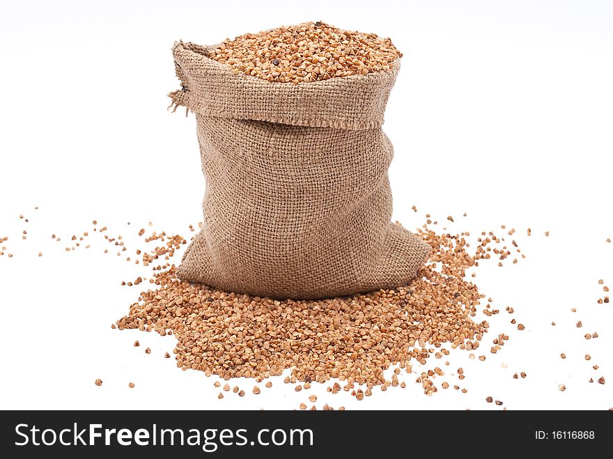 Burlap sack with buckwheat spilling on white