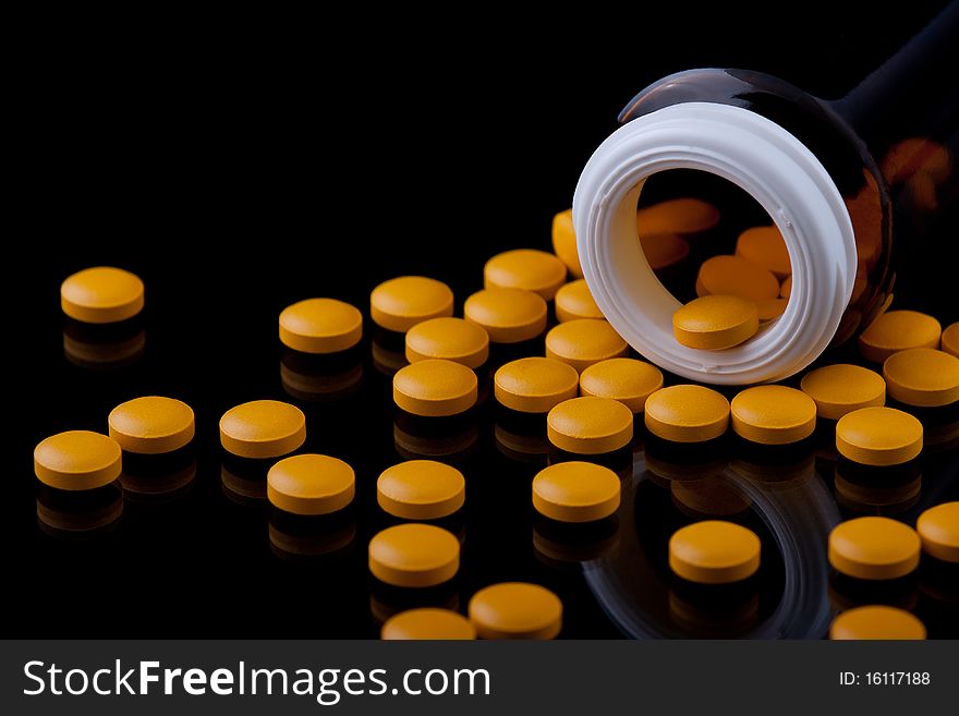 Yellow pills and a bottle on a black background