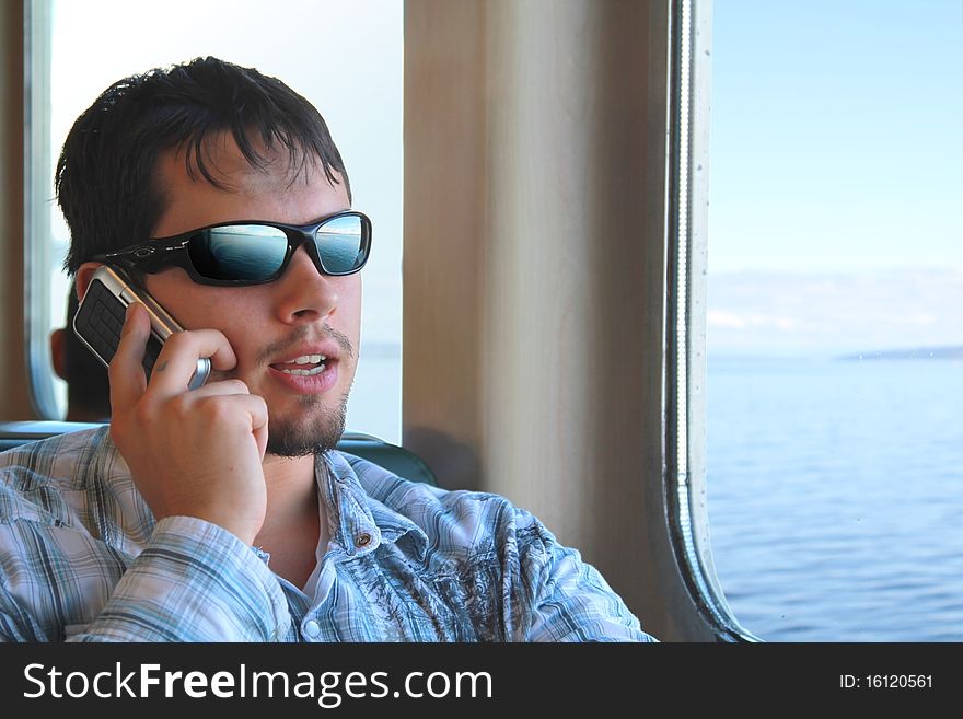 Cool guy with sunglasses talks on cell phone while commuting on a ferry. Cool guy with sunglasses talks on cell phone while commuting on a ferry