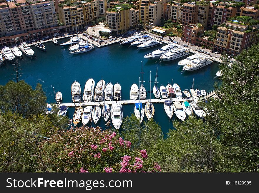 Yachts moored in a sunny marina in Monaco with surrounded by buildings.