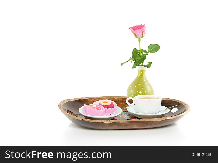 A wooden colorful tray with coffee and petit four and a rose isolated over white. A wooden colorful tray with coffee and petit four and a rose isolated over white