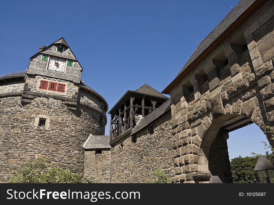 Fragment of large clock tower and city wall with a gate of the medieval fortress. Sunny morning. Schloss Burg. Germany.