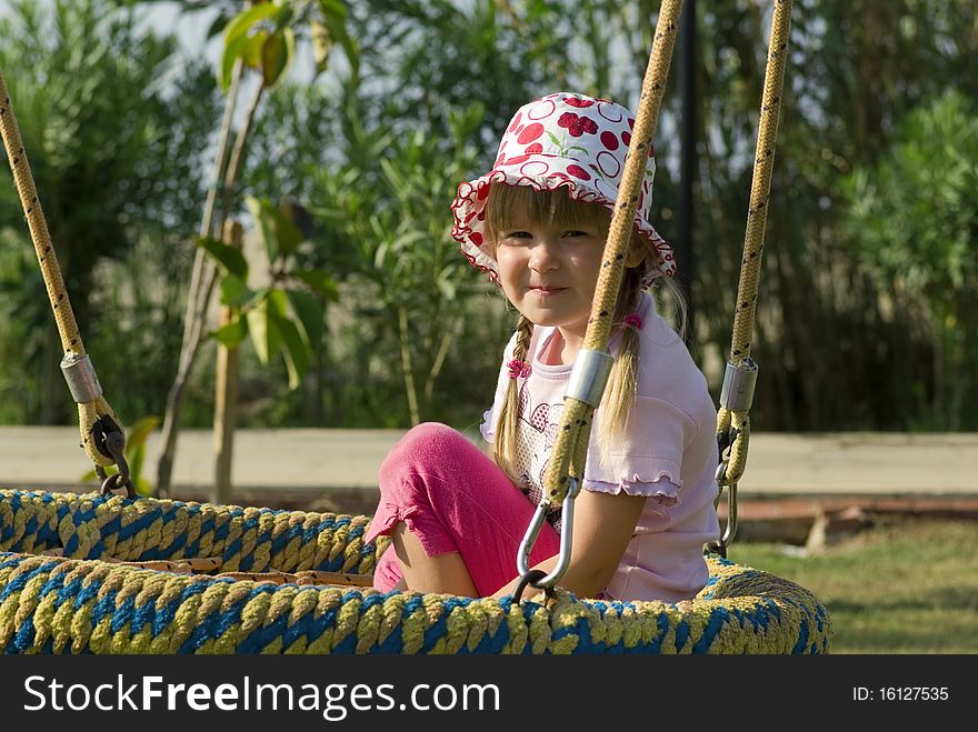 A smiling little girl sitting on a swing in a playground. A smiling little girl sitting on a swing in a playground