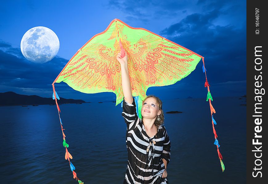 Beautiful woman with kite on the beach under moon