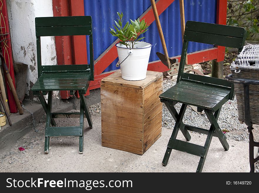 Rustic scene with two green wooden chairs and a wooden box with enamel bucket holding a plant. Rustic scene with two green wooden chairs and a wooden box with enamel bucket holding a plant