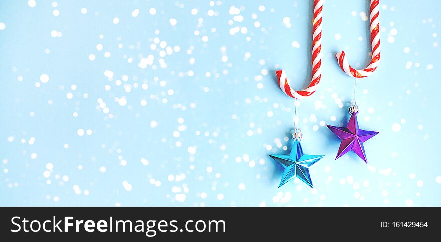 Two candy canes with toys on the Christmas tree in the form of stars on a blue background. Banner for the site. Two candy canes with toys on the Christmas tree in the form of stars on a blue background. Banner for the site.