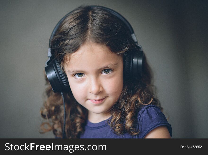 Beautiful little curly happy caucasian girl wearing headphones listening sound audio music