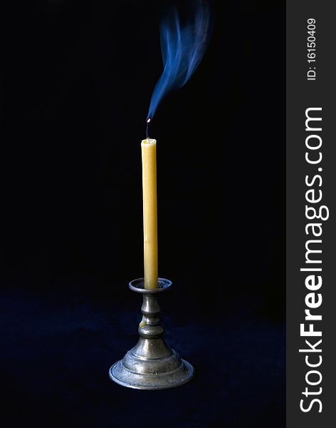 The extinct candle in a candlestick smokes on a black background. The extinct candle in a candlestick smokes on a black background.