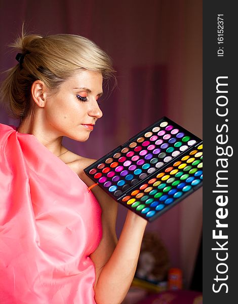 Beautiful girl holding a paintbrush and a box of colored eye shadow for make-up. Beautiful girl holding a paintbrush and a box of colored eye shadow for make-up