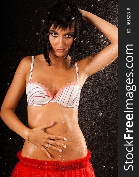 Beautiful sexual wet girl in white swimsuit and in red skirt with expressive eyes in the drops of water on the black background. Beautiful sexual wet girl in white swimsuit and in red skirt with expressive eyes in the drops of water on the black background