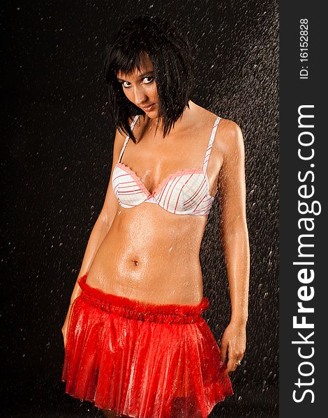 Beautiful sexual wet girl in white swimsuit and in red skirt with expressive eyes in the drops of water on the black background. Beautiful sexual wet girl in white swimsuit and in red skirt with expressive eyes in the drops of water on the black background