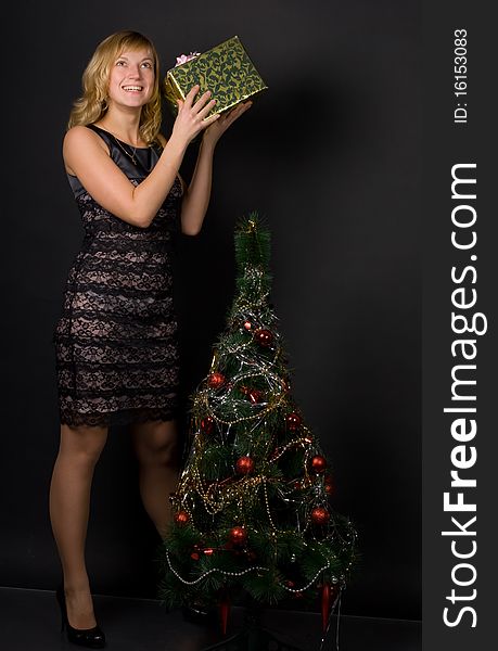 The beautiful girl with a gift near a Christmas tree on a black background. The beautiful girl with a gift near a Christmas tree on a black background