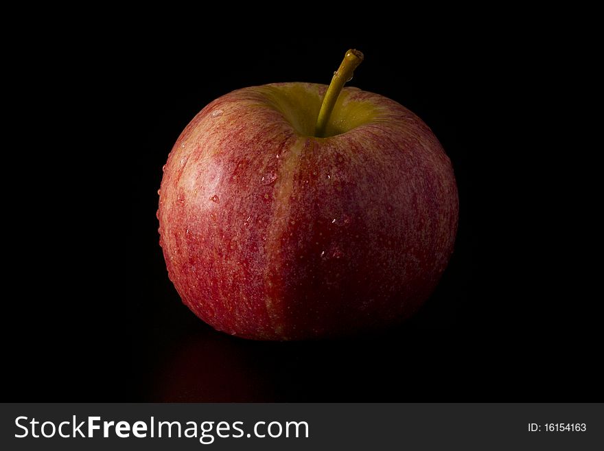 A red apple with water droplets on a black background.