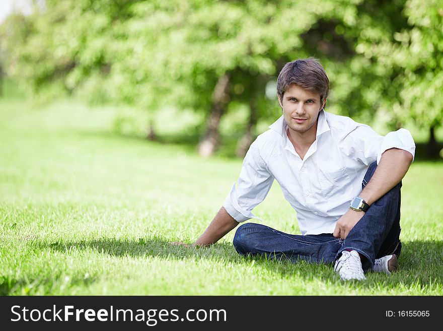 A young handsome man sits on the lawn. A young handsome man sits on the lawn