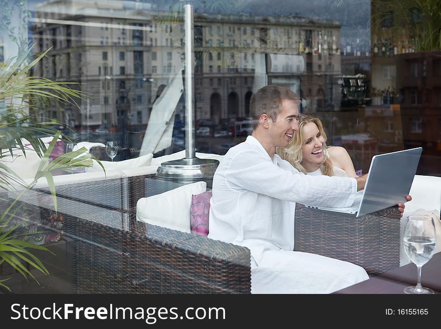 Laughing young couple looking at laptop in a restaurant. Laughing young couple looking at laptop in a restaurant