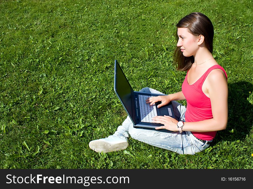 Young pretty woman with laptop sitting on green lawn in a park. Young pretty woman with laptop sitting on green lawn in a park