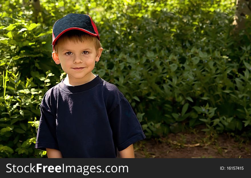 A cute little boy outside standing in a sunny camping area, surrounded by green bushes and trees. A cute little boy outside standing in a sunny camping area, surrounded by green bushes and trees.