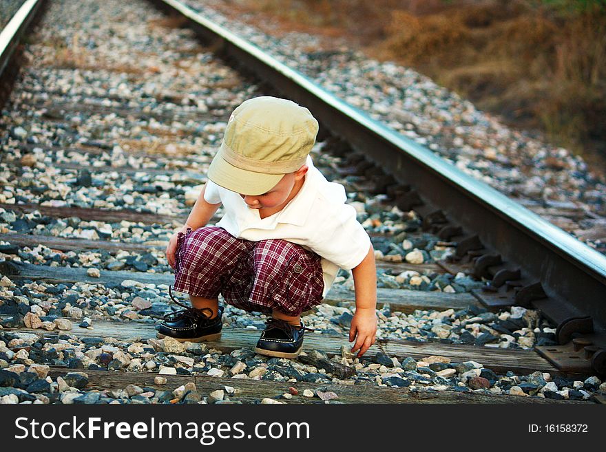 Curious Boy on train tracks with hat picking up rocks