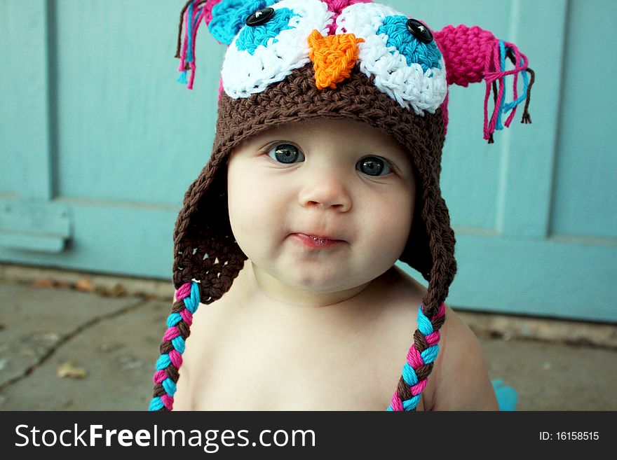 A cute baby girl sitting surrounded with a blue frilly skirt and hat.