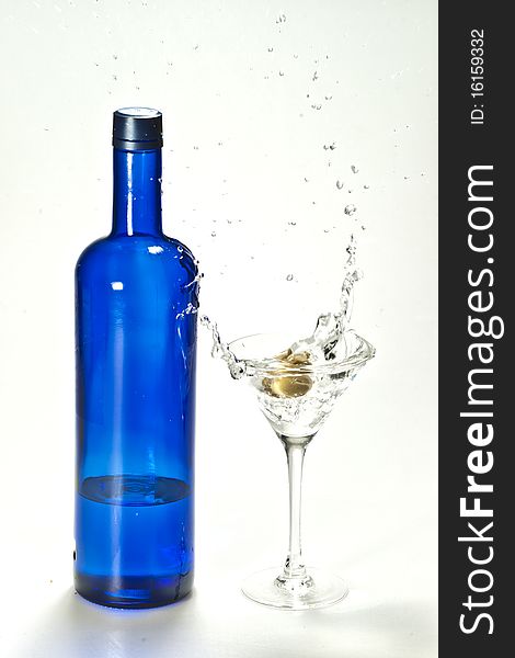 A splash of martini made by olive with a blue bottle of vodka