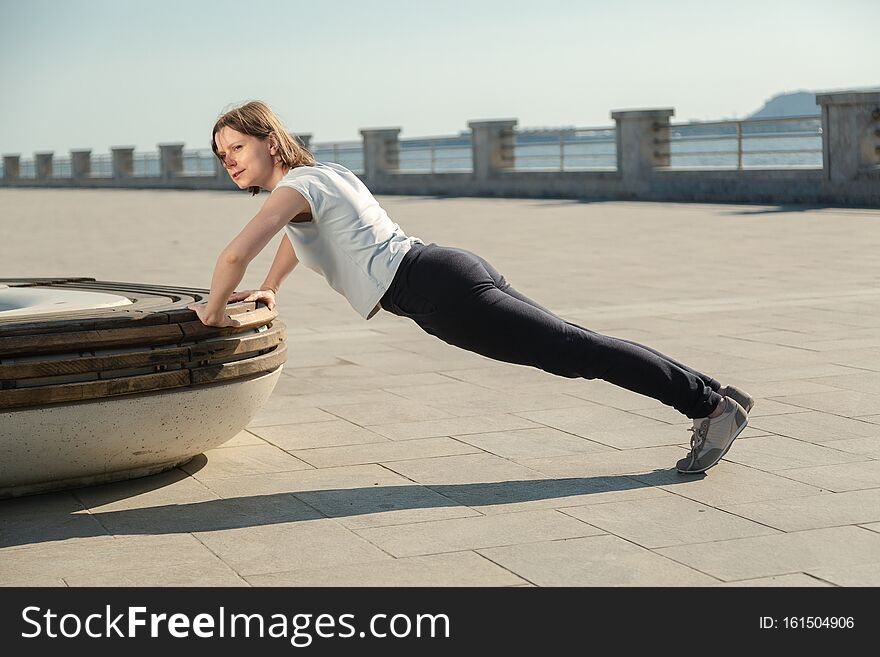 Young woman doing sport exercises outside with bench