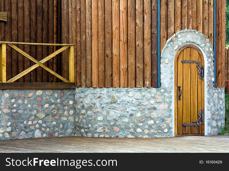 Part of a wall of a building from a tree and stones with a wooden door. Part of a wall of a building from a tree and stones with a wooden door