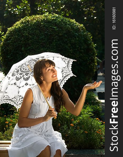 Surprised young pretty girl with white sun umbrella sitting on the bench in the park. Surprised young pretty girl with white sun umbrella sitting on the bench in the park