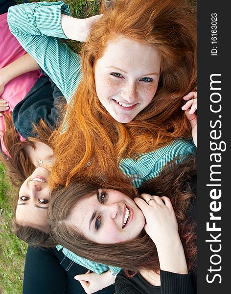 Three different girls are sitting on the grass smiling and hugging in a spring daytime. Three different girls are sitting on the grass smiling and hugging in a spring daytime