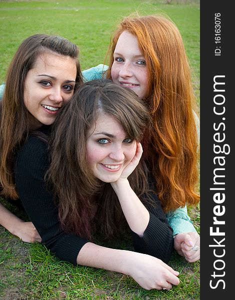 Three different girls are sitting on the grass smiling and hugging in a spring daytime. Three different girls are sitting on the grass smiling and hugging in a spring daytime