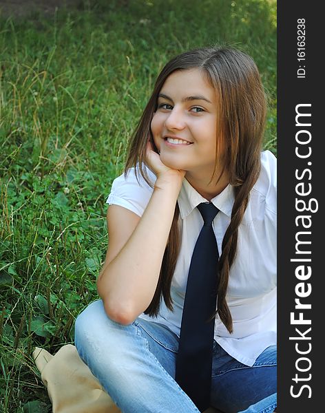 Beautiful student girl is smiling and seating on the grass