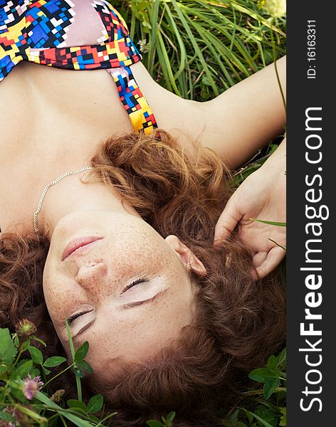 Beautiful ginger girl is lying in the green grass with closed eyes