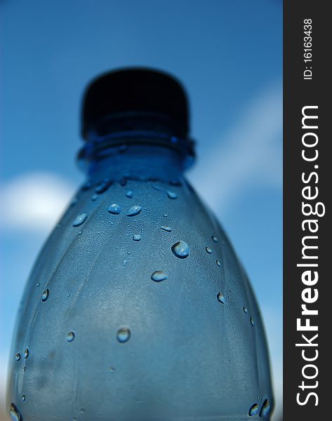 Bottle with drops of water with blue sky with some clouds on the background. Bottle with drops of water with blue sky with some clouds on the background.