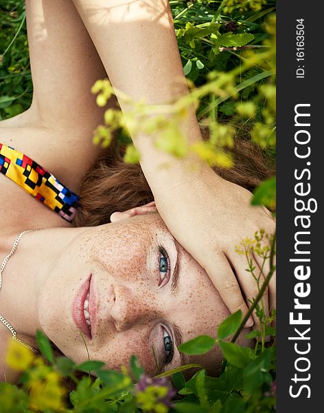 Beautiful ginger girl is lying in the green grass